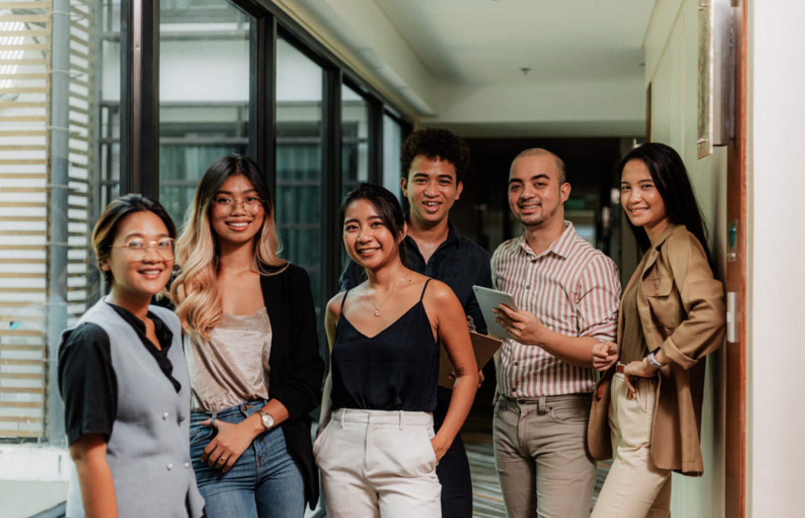 A team of young Filipino professionals smiling together in an office hallway